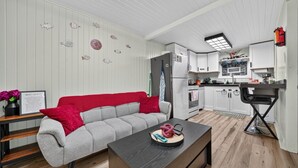 A modern living room with a grey sofa, a coffee table, and a kitchen area with white cabinets and a black countertop.
