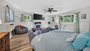 A bedroom with a bed, a fireplace, a ceiling fan, and a window with curtains.