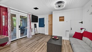A cabin interior with a wooden floor, a grey sofa, a small table, and a TV mounted on the wall.