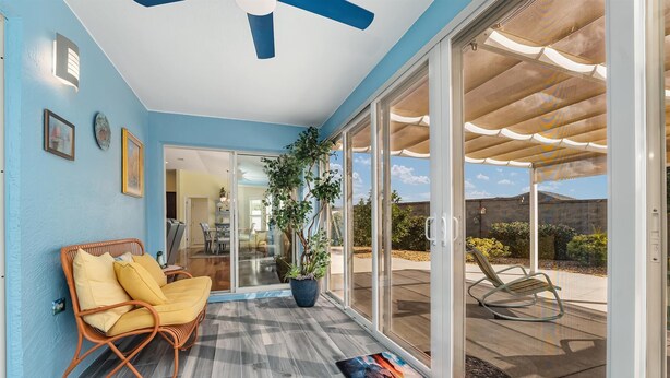 A spacious patio with a wicker chair and a potted plant, a sliding glass door leading to an outdoor area, and a ceiling fan. - Charming Courtyard Villa - 3-bedroom house with AC in The Villages (The Villages)