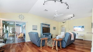 A spacious living room with a wooden floor, a ceiling fan, a bookshelf, and a television. - Charming Courtyard Villa - 3-bedroom house with AC in The Villages (The Villages)