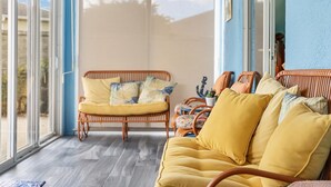 A room with a yellow sofa, wicker chairs, and a view through a large window. - Charming Courtyard Villa - 3-bedroom house with AC in The Villages (The Villages)