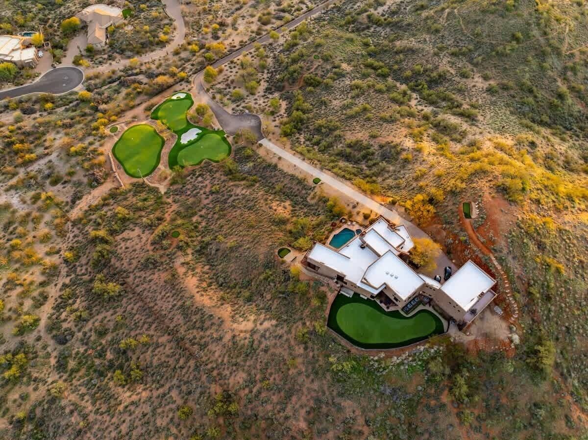 Vue aérienne d’une maison moderne dotée d’une piscine, entourée d’espaces aménagés et d’un paysage désertique.