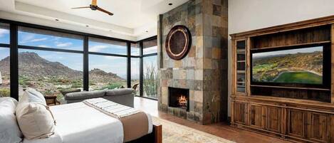 A bedroom with a large bed, a fireplace, a television, and a view of a mountainous landscape.