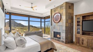 A bedroom with a large bed, a fireplace, a TV, and a view of the mountains.