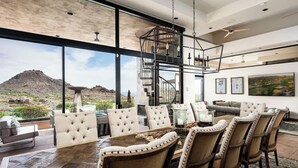 A spacious dining area with a high ceiling, large windows, and a view of a mountainous landscape.