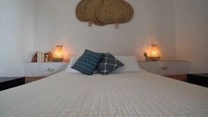 Ein Bett mit weißer, gesteppter Bettdecke, zwei Nachttische mit Lampen und zwei gewebte Wandbehänge.