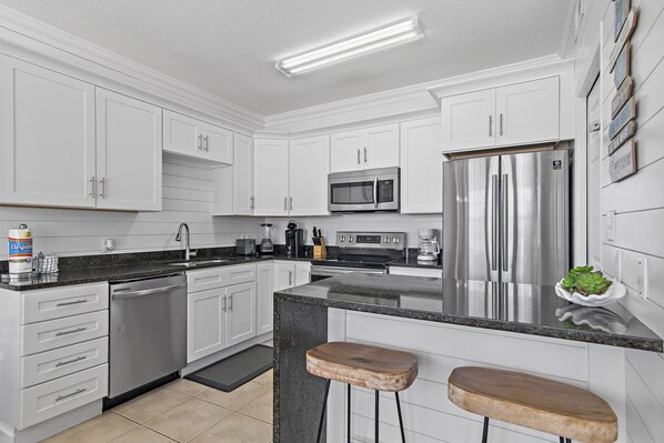 A modern kitchen with white cabinets, stainless steel appliances, and a granite countertop.