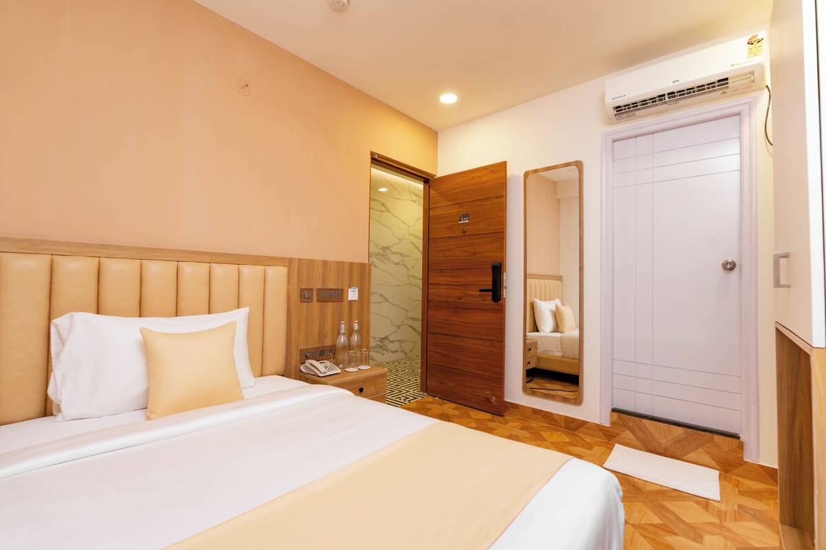 A hotel room with a large bed, a wooden wardrobe, a mirror, and a door.