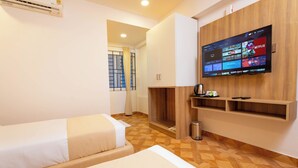 A hotel room with a TV displaying streaming services, a bed, a small table with a cup, and a trash can. - U by Z Hotels, Seshadripuram (Bengaluru)