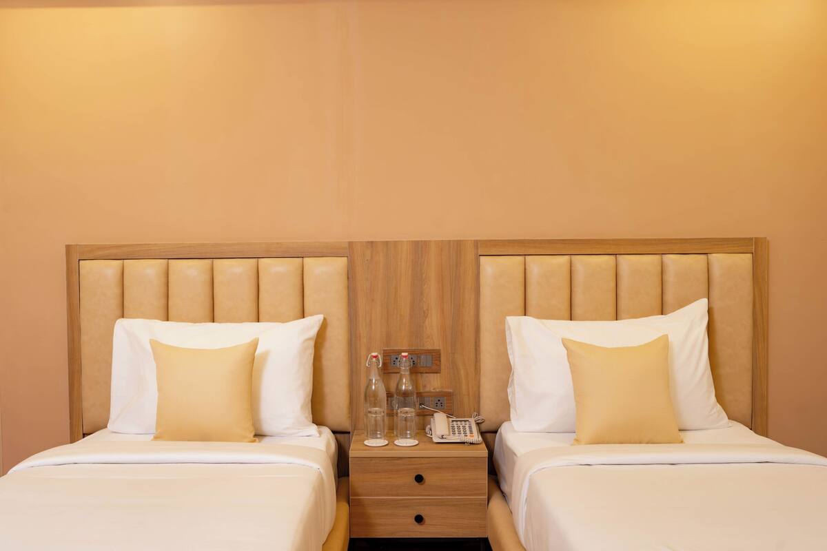 A hotel room with two beds, each with a wooden headboard and white bedding. There is a nightstand between the beds with a telephone, two bottles, and a power outlet.