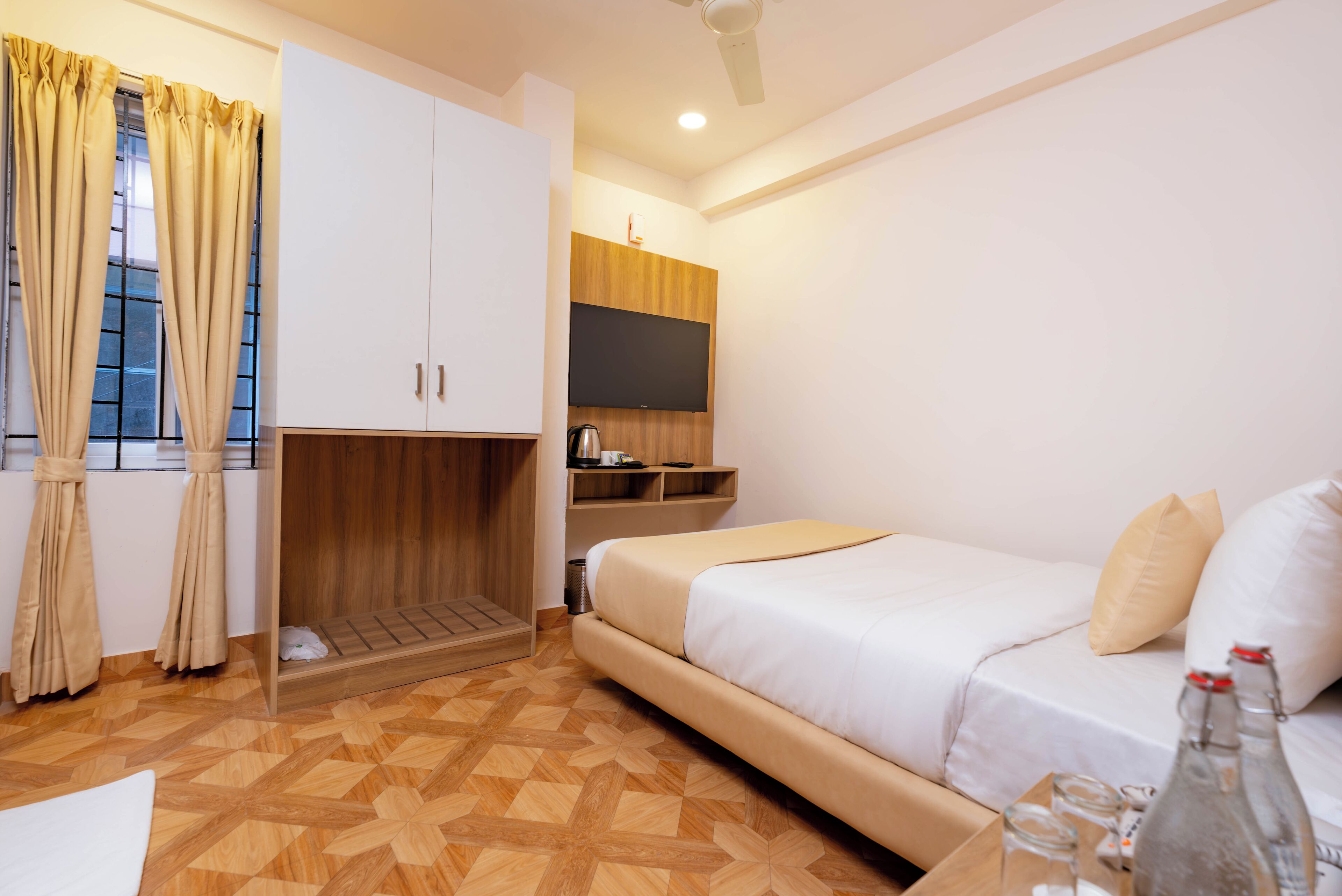 Una habitación de hotel con una cama, televisión, armario de madera y ventana con cortinas.