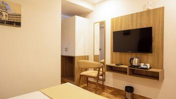 Una habitación de hotel con una cama, un mueble de televisión de madera, un espejo, una silla y un pequeño estante con artículos de aseo.