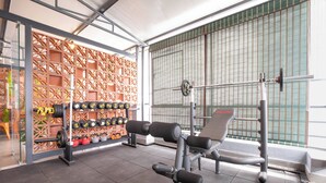 A gym with weightlifting equipment, a wall of dumbbells, and a window with blinds. - U by Z Hotels, Seshadripuram (Bengaluru)