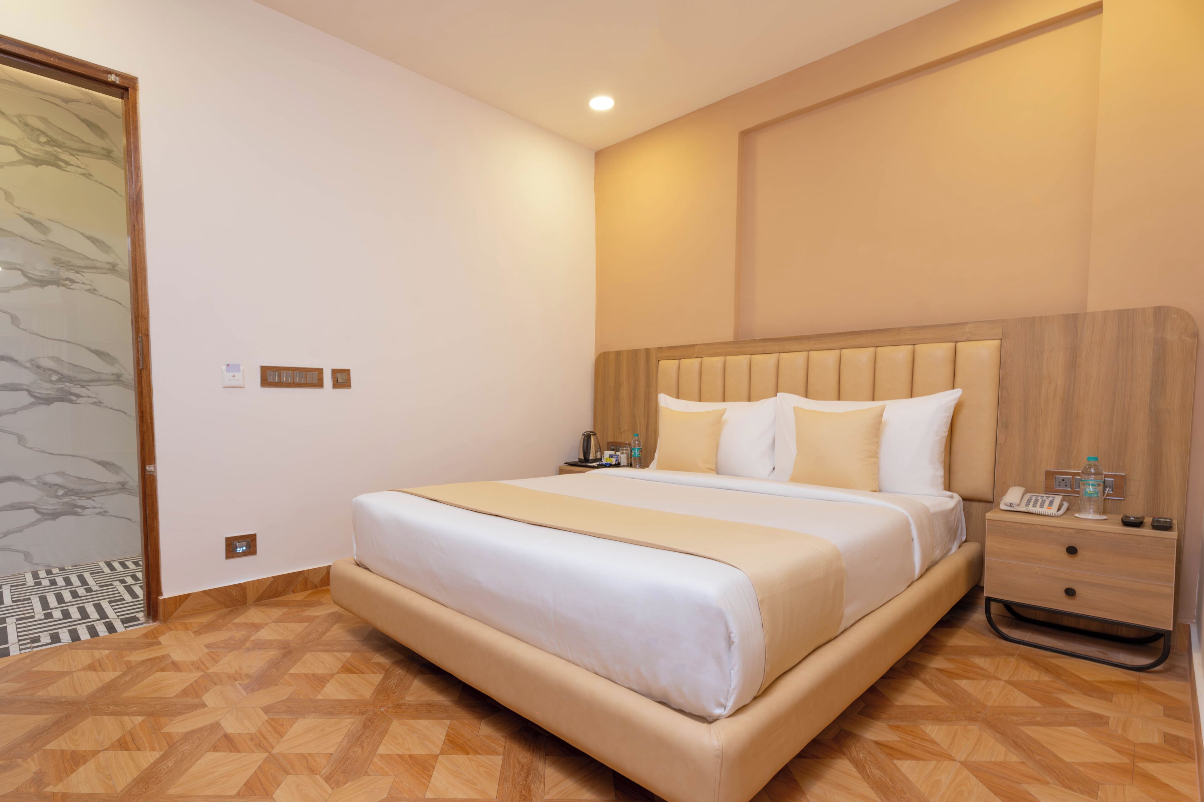 Una habitación de hotel moderna con una cama grande, cabecera de madera, mesitas de noche y suelo con estampado.