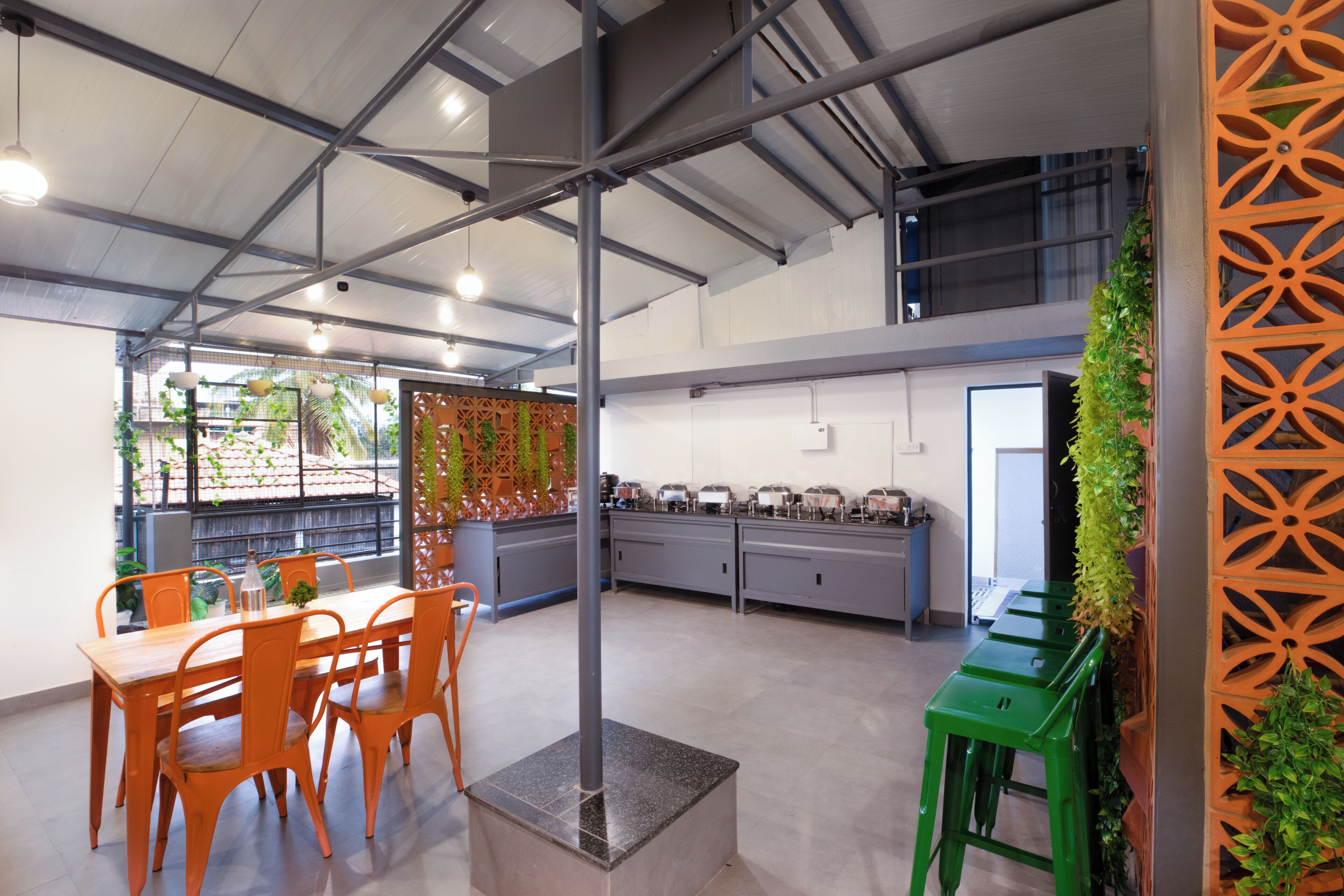 Una cocina moderna con techo alto, conductos a la vista y un comedor con sillas anaranjadas y una mesa de madera.