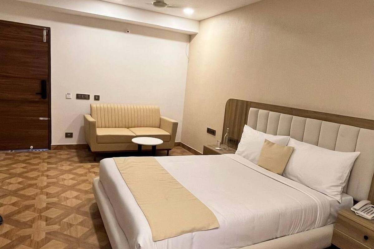 A hotel room with a large bed, a sofa, a bedside table, and a wooden floor pattern.