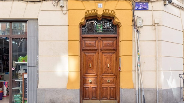A double wooden door with a decorative arch above it, a blue sign above the door, and a small window to the left.