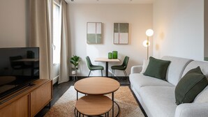 A modern living room with a flat-screen TV, a sofa, a coffee table, and a dining area with chairs and a small table. - Sandoval - Superior 1 Bedroom with Sofa Bed (Madrid)