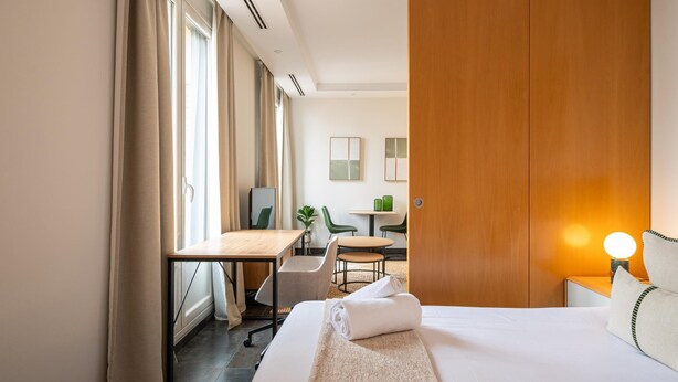 A hotel room with a large bed, a desk, a chair, and a small table with a lamp. - Sandoval - Superior 1 Bedroom with Sofa Bed (Madrid)