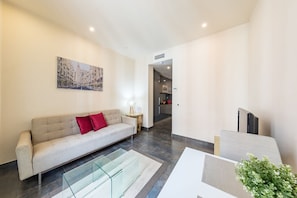 A modern living room with a sofa, a glass coffee table, and a painting on the wall. - Sandoval - 1 Bedroom with Sofa Bed (Madrid)
