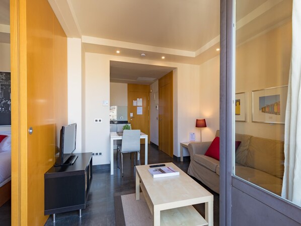 A modern hotel room with a bed, a desk, a chair, a sofa, and a small table.