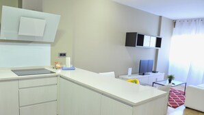 A modern kitchen with white cabinetry, a built-in island, and a flat-screen TV mounted on the wall. - Goya - 1 Bedroom Apartment (Madrid)