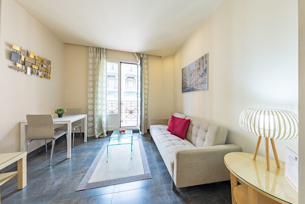 A modern living room with a sofa, a glass coffee table, a dining table with chairs, and a decorative wall piece. - Sandoval - 1 Bedroom with Sofa Bed (Madrid)
