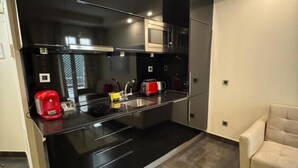 Une cuisine moderne avec des plans de travail noirs, des appareils en acier inoxydable et un fauteuil beige.