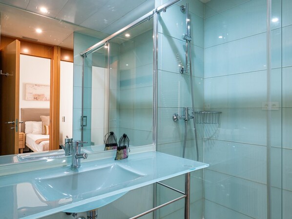 A modern bathroom with a glass shower enclosure, a large mirror, and a glass sink.