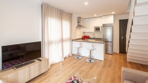 A modern apartment with a living room, kitchen, and dining area. It includes a flat-screen TV, a kitchen with a microwave and refrigerator, and a dining area with bar stools.