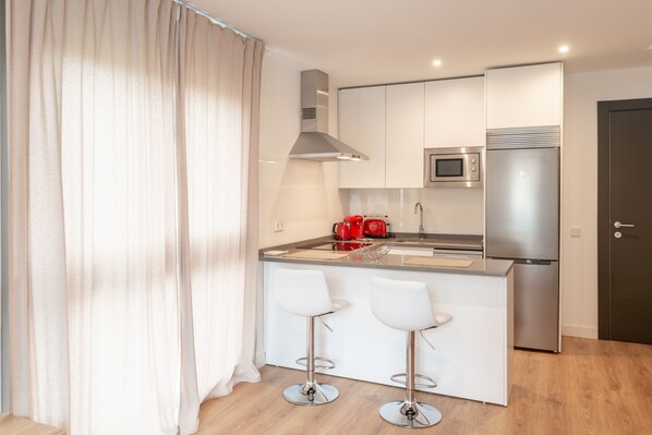 A modern kitchen with a central island, stainless steel appliances, and white bar stools.