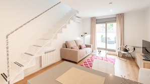 A modern living room with a staircase, a sofa, a TV, and a dining area.