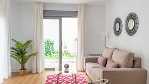 A modern living room with a sofa, a glass coffee table, a potted plant, and a view of the outdoors.