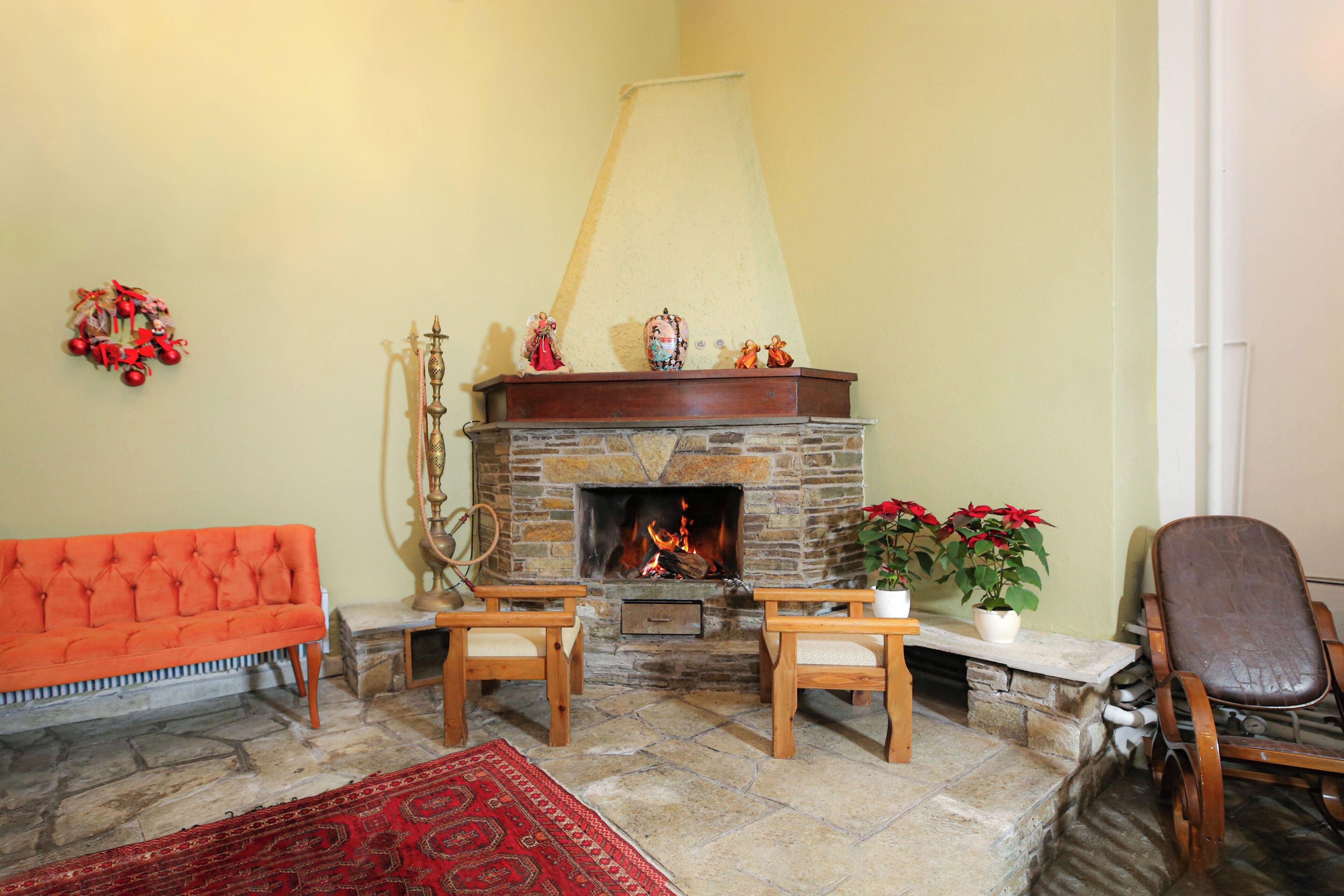 Una sala de estar acogedora con chimenea de piedra, un sofá rojo, dos sillas de madera, un tapete rojo y una planta en maceta.