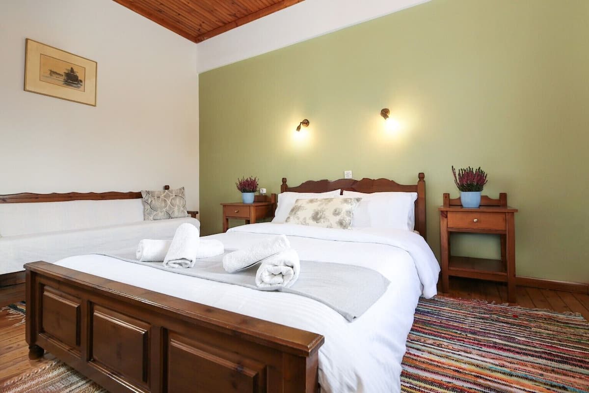 A hotel room with a large bed, two bedside tables with lamps, a wooden headboard, a green accent wall, and a framed picture on the wall.