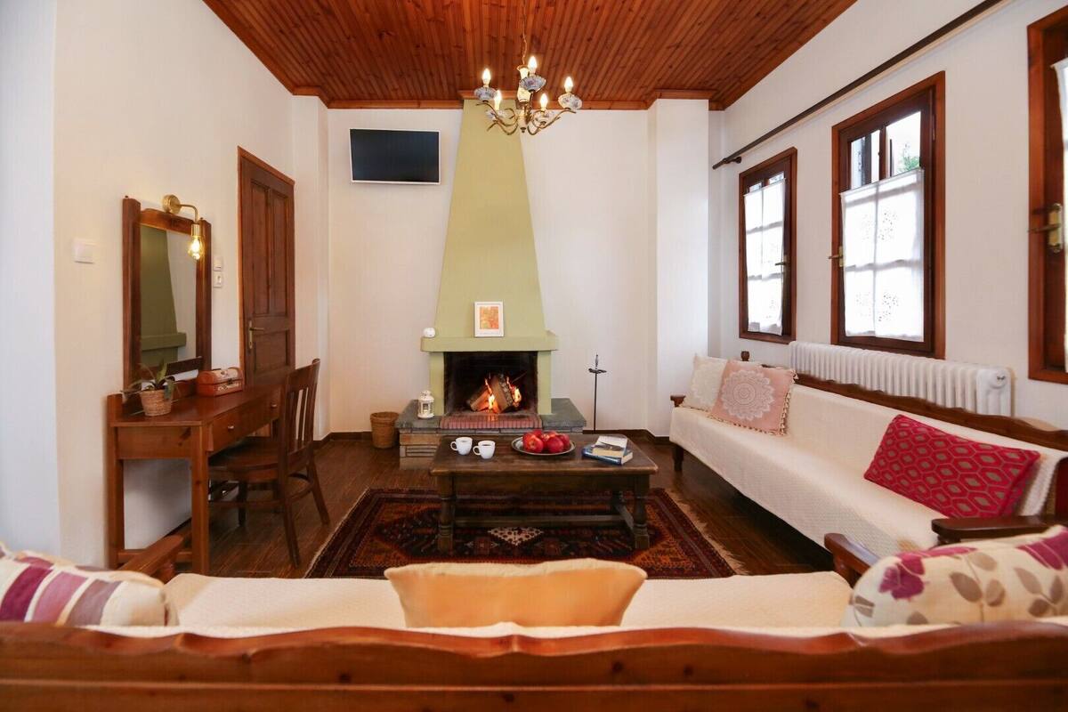 A cozy living room with a fireplace, wooden furniture, and a sofa with patterned cushions.