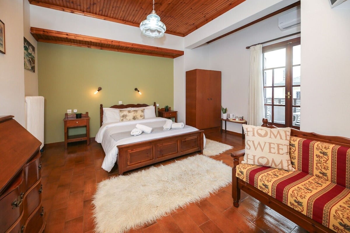 A bedroom with a wooden bed, a fluffy rug, a sofa with patterned cushions, and a window with curtains.
