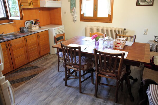 A wooden dining table with four chairs, a kitchen area with wooden cabinets, a window, and a radiator.