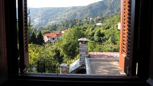 Vista desde una ventana con contraventanas abiertas, sobre un cerro con casas y vegetación.