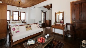 Una habitación acogedora con techo de madera, una cama con almohadas florales, un escritorio de madera con un espejo y una mesa de centro con manzanas y libros.