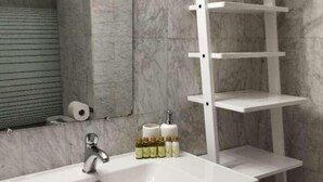 Une salle de bain avec un lavabo blanc, des murs en marbre et une étagère blanche.