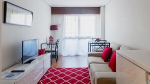 Un salon de taille modeste comprenant un téléviseur, un canapé, une table à manger et un tapis rouge à motifs.