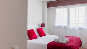 Une chambre d’hôtel avec un lit, des oreillers rouges, une couverture rouge et une fenêtre avec des rideaux légers.