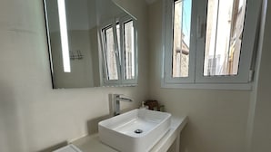 Un baño con lavamanos blanco, espejo y ventana.