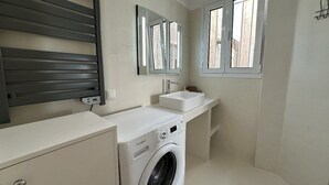 Un baño moderno y compacto con lavadora integrada, un lavabo y un espejo.