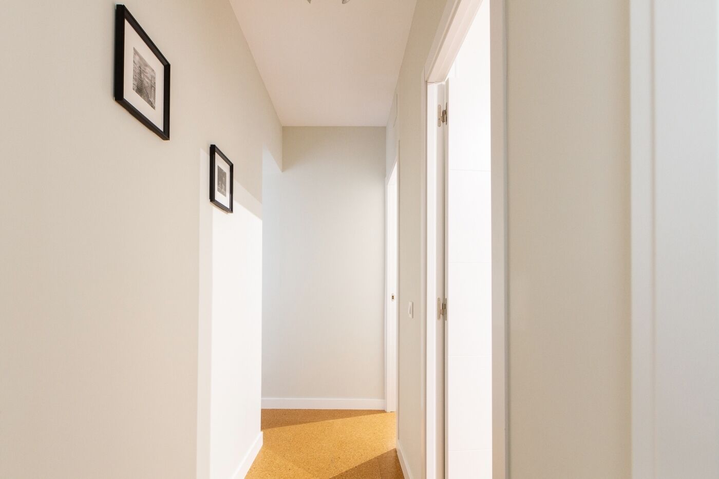 Un couloir aux murs blancs, orné de deux tableaux encadrés, et une porte au fond.
