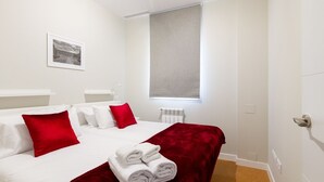 A hotel room with a bed, white walls, a window with a blind, a radiator, and a framed picture on the wall. - Ibiza - Parque del Retiro- 2 Bedrooms (Madrid)