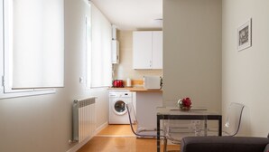 A compact kitchen with a washing machine, a microwave, and a small dining area with a glass table and chairs. - Ibiza - Parque del Retiro- 2 Bedrooms (Madrid)