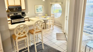 A compact kitchen with modern appliances, a dining area with white chairs, and a view of the parking lot through a door. - ⨳ Lake Erie Waterfront condo conveniently located near Jet Express - 1BR 1 BA ⨳ (Port Clinton)
